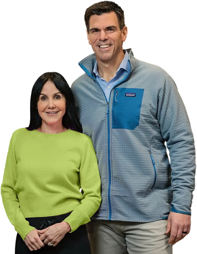 A woman in a lime green sweater stands next to a man in a gray zip-up jacket with a blue pocket; both are smiling and looking at the camera, representing a top kitchen remodeling company in Columbus, Ohio.