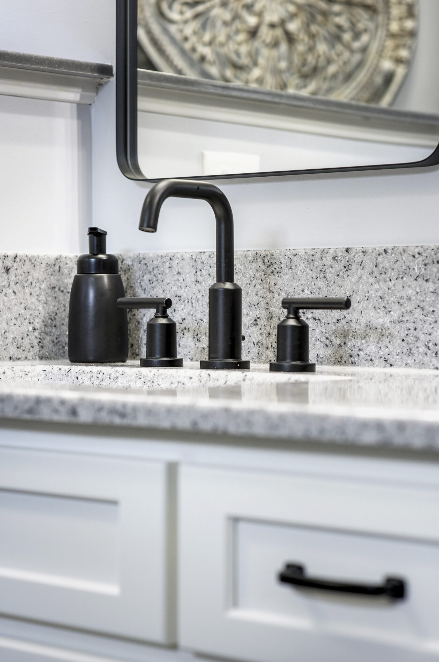 Close-up of a modern bathroom sink with granite countertop, black faucet, soap dispenser, and drawer with a black handle—showcasing the quality work of a leading bathroom remodeling company in Columbus, Ohio. A large mirror is partially visible above the sink.