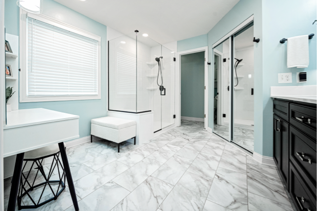 Modern bathroom with light blue walls, marble floor tiles, a glass-enclosed shower, black vanity cabinets, and mirrors reflecting the space—an inspiring design by a top bath remodel and bathroom remodeling company in Columbus, Ohio.