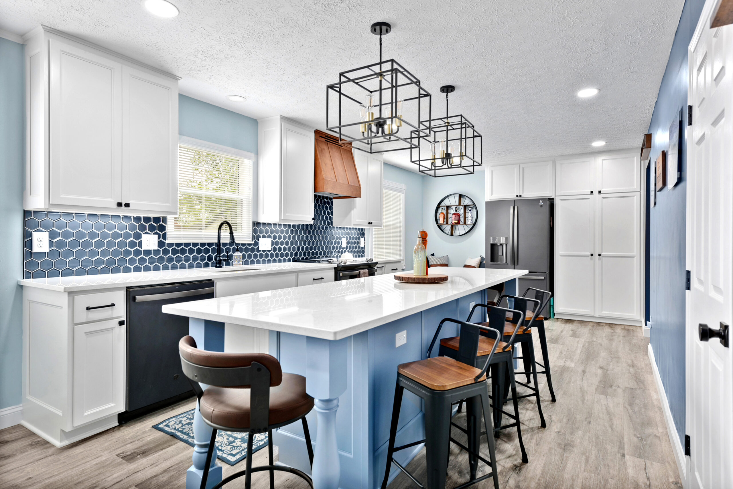 Modern kitchen remodel with a large white island, black and wood barstools, blue hexagon tile backsplash, white cabinets, black appliances, and geometric pendant lights—crafted by a top kitchen remodeling company in Columbus, Ohio.
