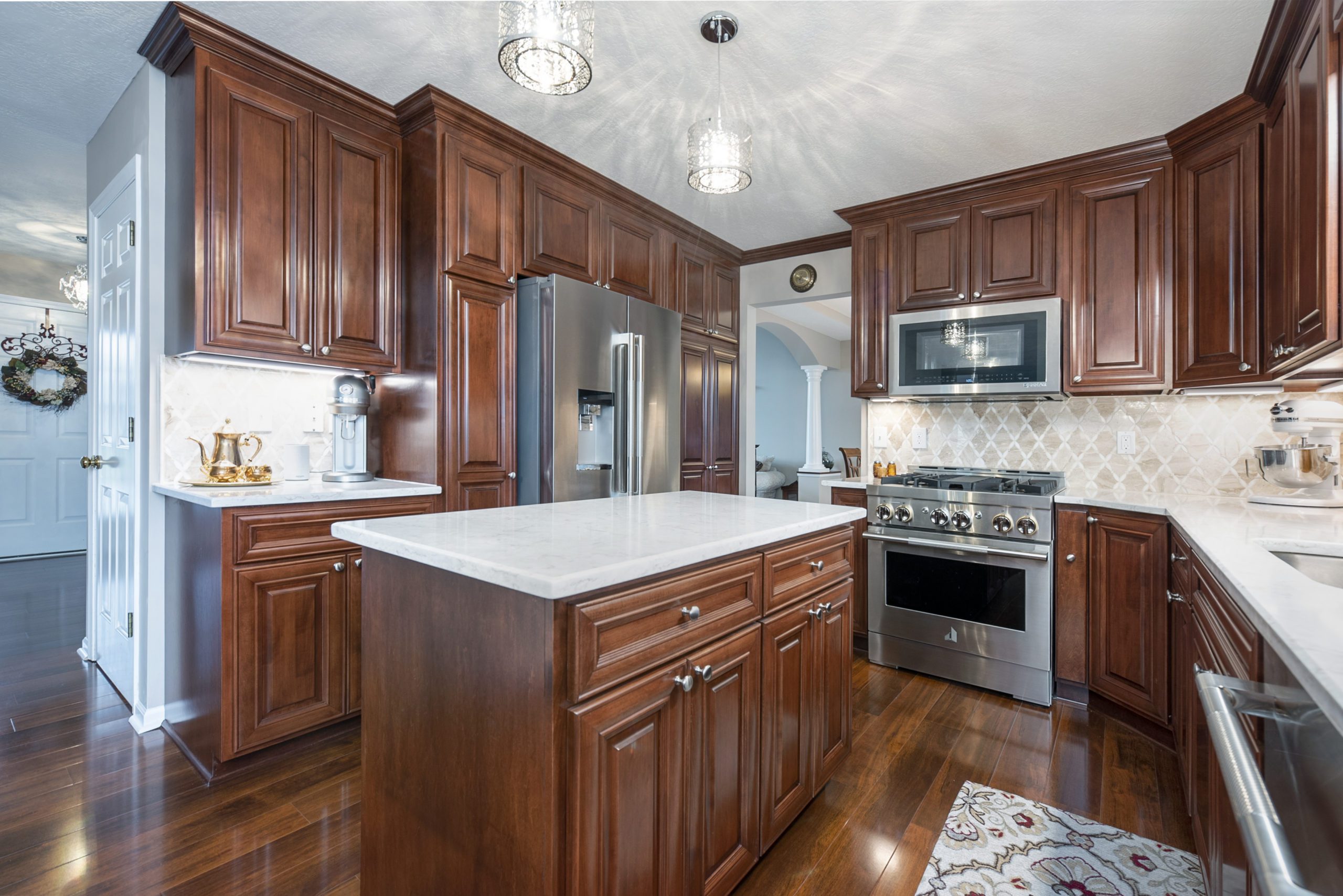 Spacious kitchen with dark wood cabinets, stainless steel appliances, a center island with marble countertop—perfect inspiration from a top kitchen remodel. Light fixtures hang above, and a decorative rug lies by the sink.