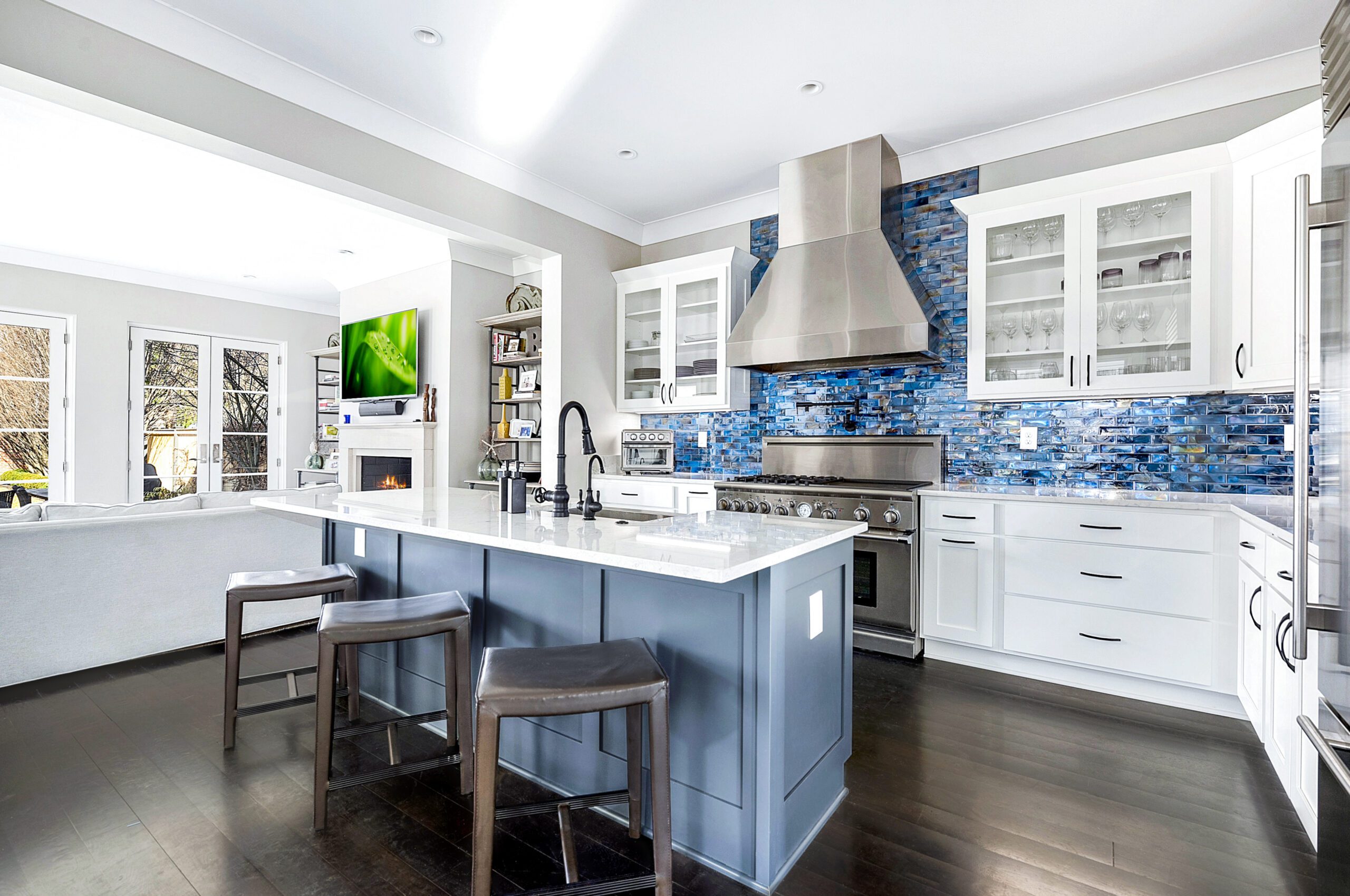 Modern kitchen renovation with white cabinets, a large stainless steel stove, blue mosaic tile backsplash, and a gray island with two barstools. Trust our kitchen remodeling company Columbus Ohio for open layouts flowing into bright living areas.