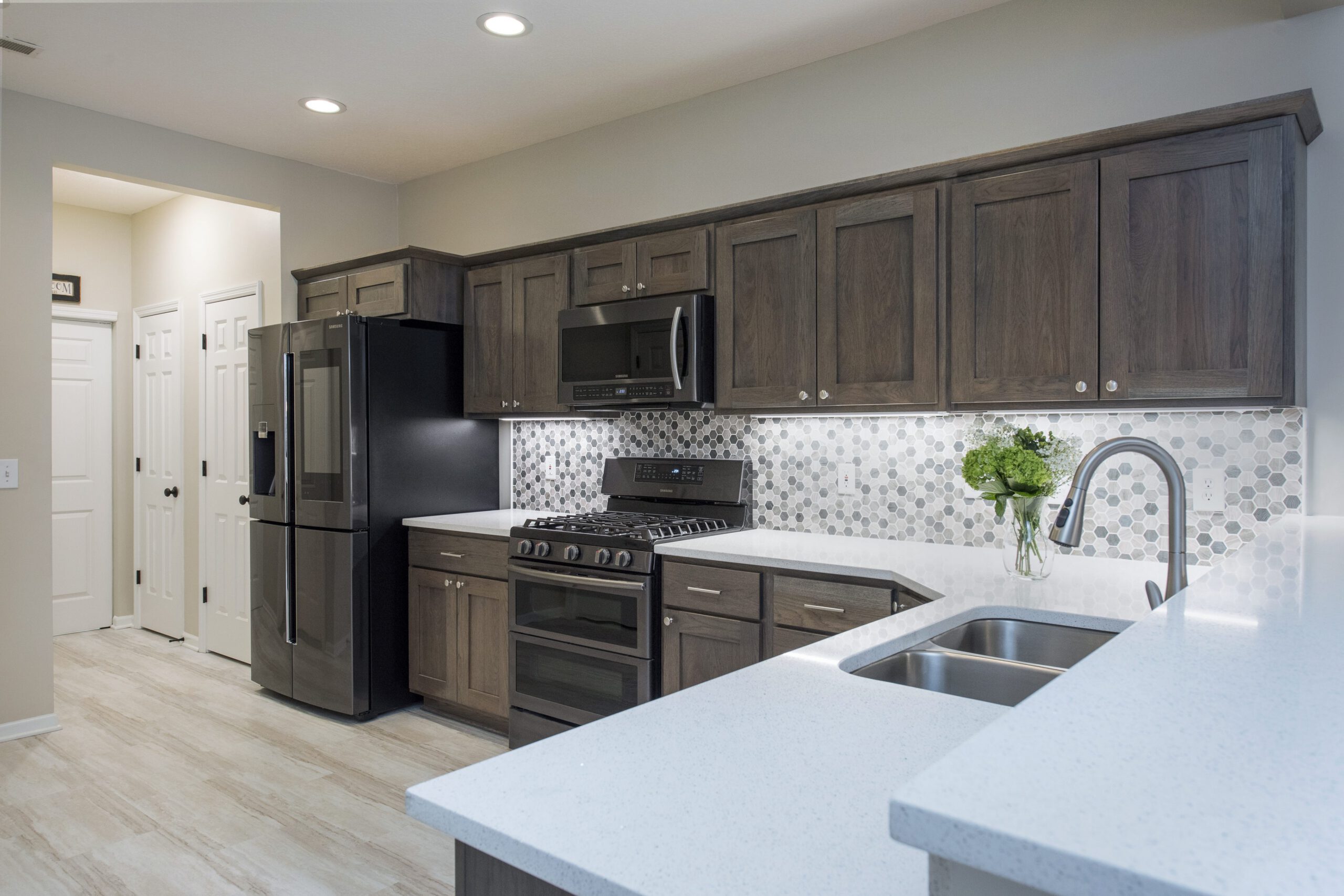 Modern kitchen remodel with dark wood cabinets, stainless steel appliances, white quartz countertop, hexagonal tile backsplash, and a sink with green flowers. Recessed lighting brightens the space by a leading kitchen remodeling company Columbus Ohio.
