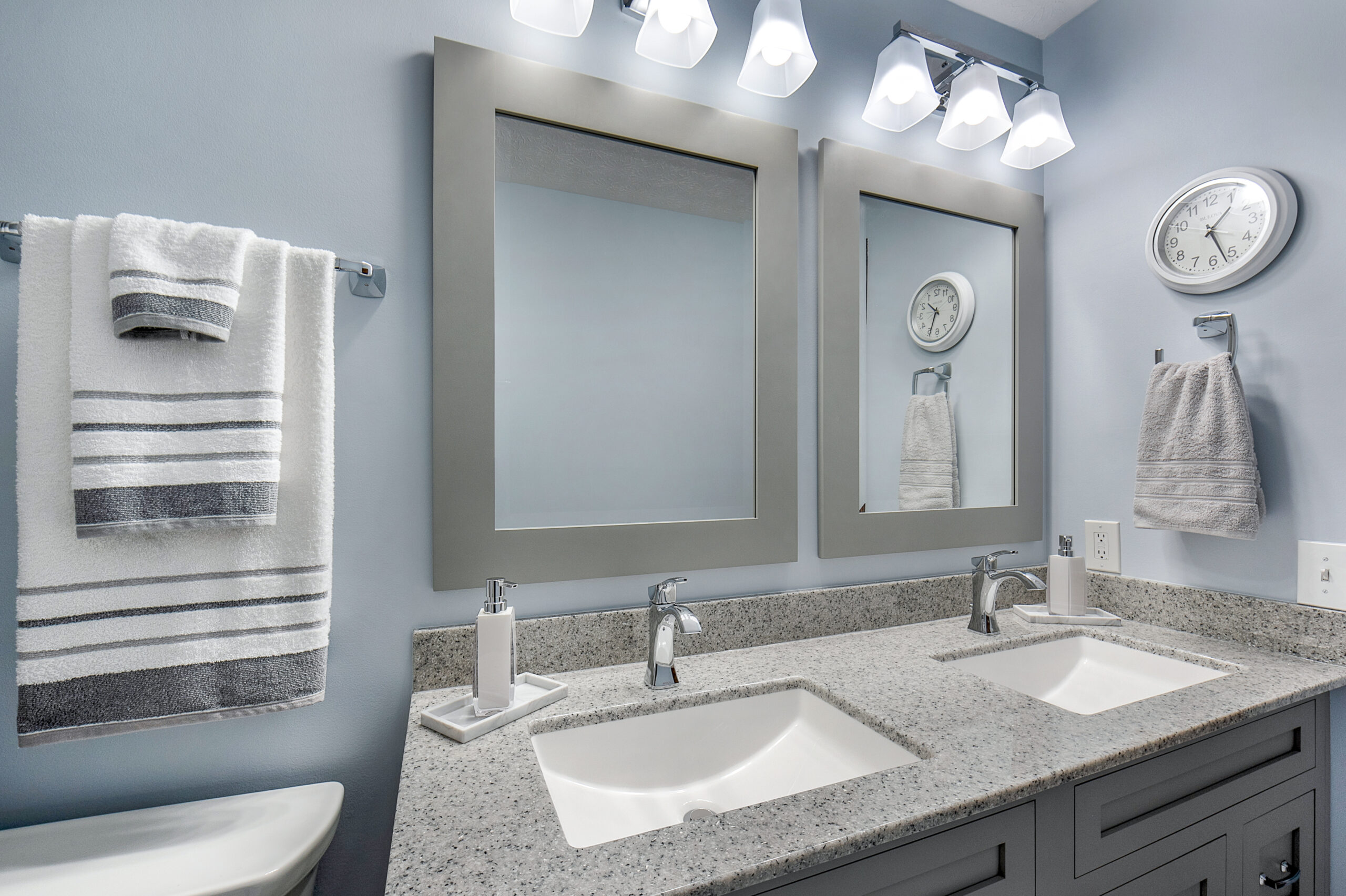 Modern bathroom with a double sink vanity, two large mirrors, chrome fixtures, stylish towels, a wall clock, and light gray tones—expertly crafted by a leading bathroom remodeling company in Columbus, Ohio.