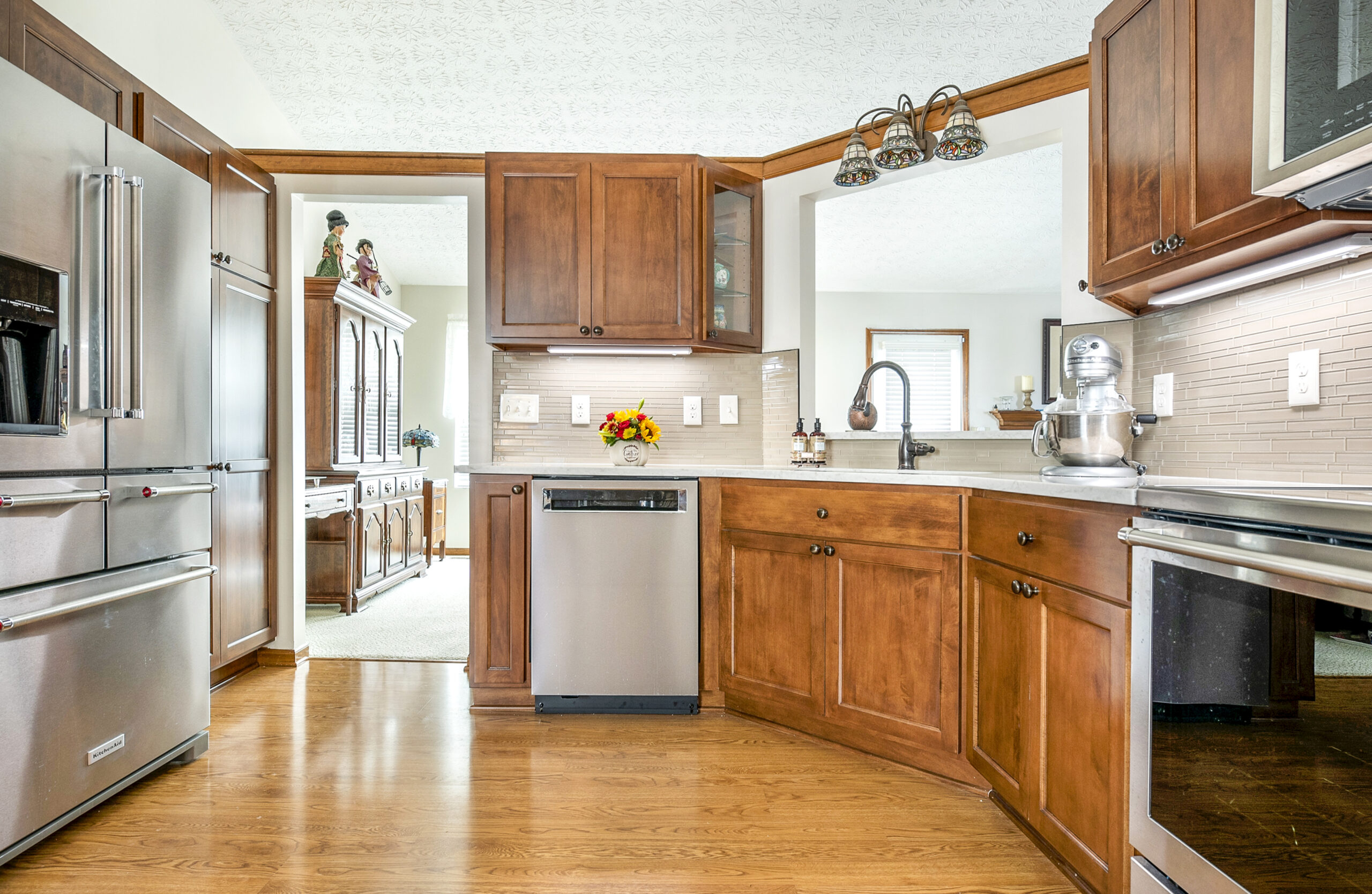 A spacious kitchen with wooden cabinets, stainless steel appliances, light countertops, and a hardwood floor. Expertly renovated by a leading kitchen remodeling company Columbus Ohio, the adjoining dining room is visible through an open doorway.