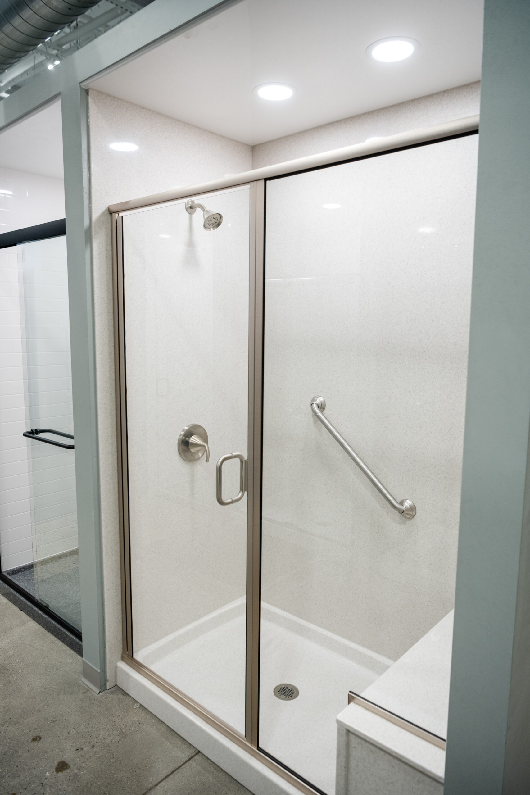Modern shower with a glass door, metal grab bar, showerhead, control handle, and small step inside. Clean white walls and recessed lights add style—a perfect example of bathroom renovation by a leading bathroom remodeling company in Columbus, Ohio.