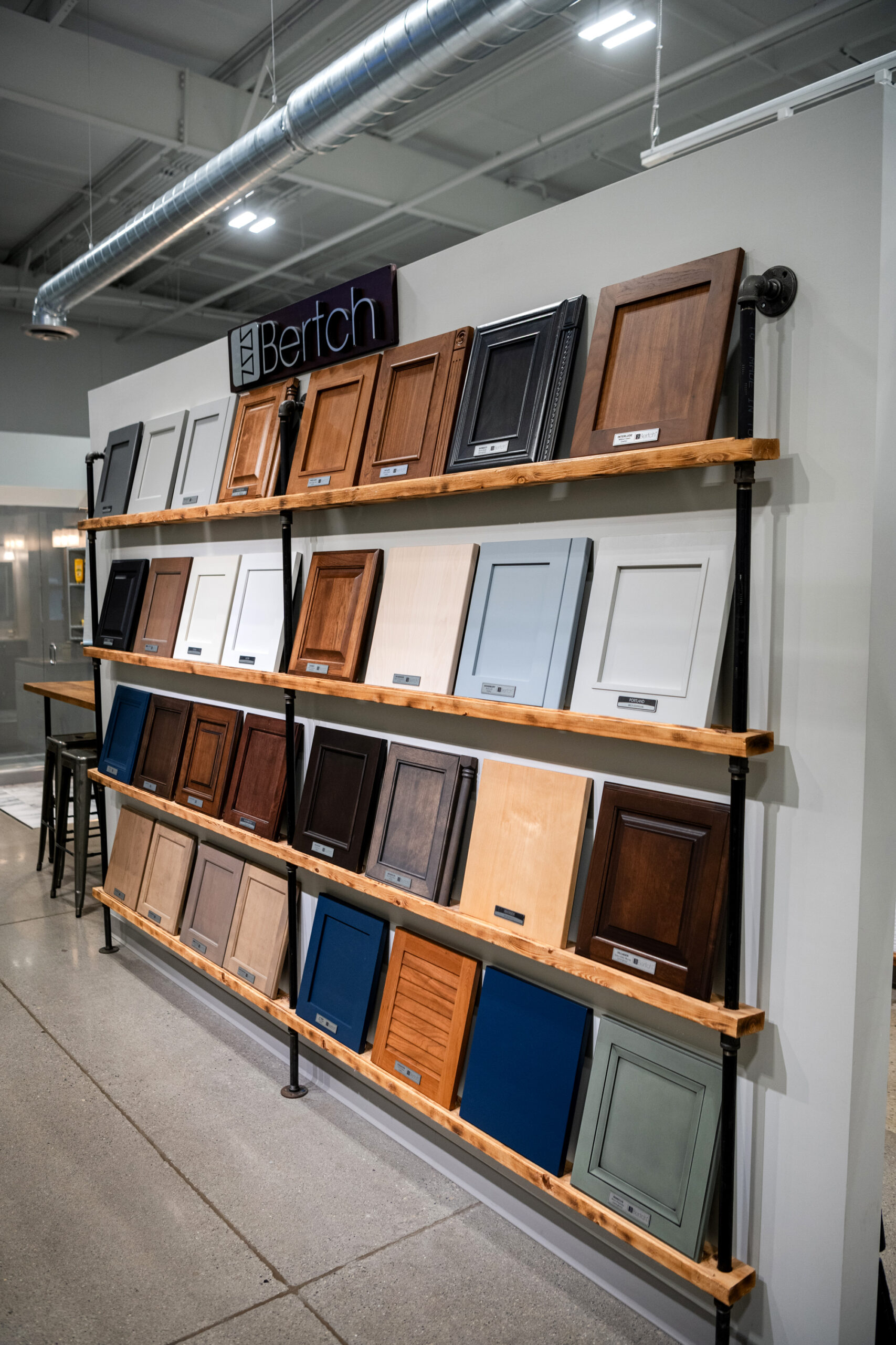 A display wall of cabinet door samples in various colors and finishes, arranged on three wooden shelves under a sign that reads Bertch, highlights the options available from a leading kitchen remodeling company in Columbus, Ohio.