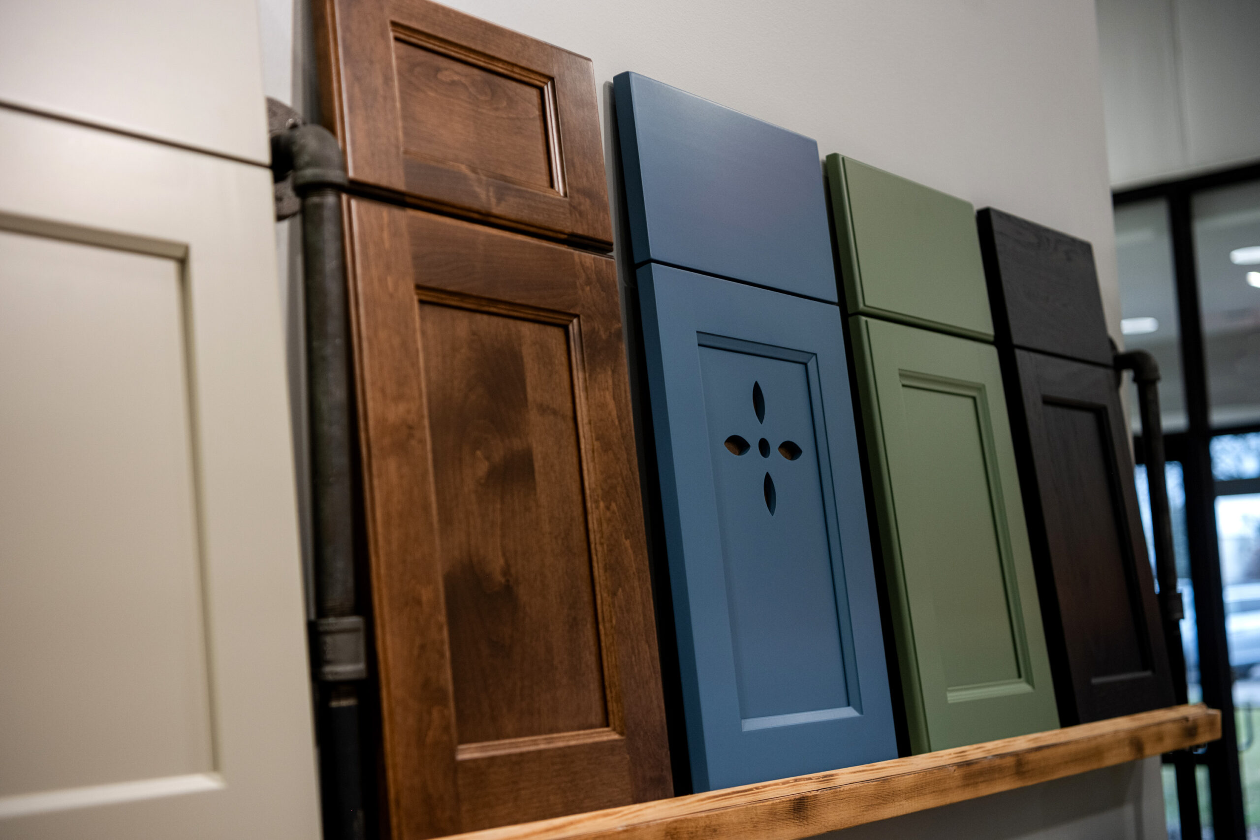 A row of five cabinet doors in various colors and styles is displayed on a wooden shelf against a white wall, showcasing options from a leading kitchen remodeling company in Columbus, Ohio—perfect inspiration for your next kitchen remodel.