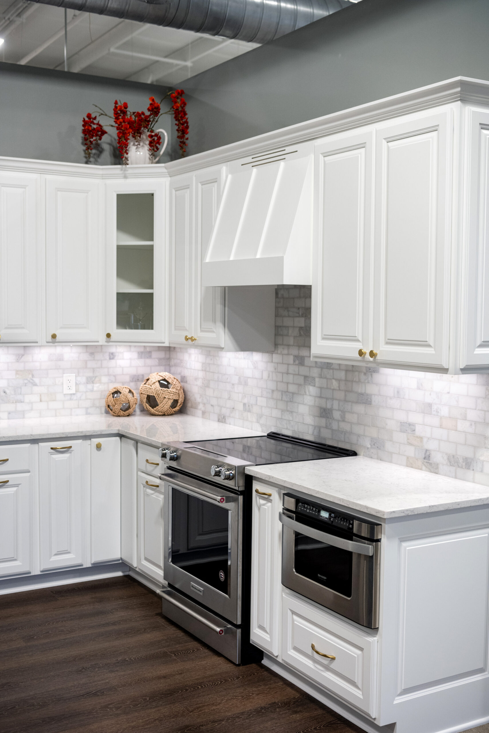 Modern kitchen with white cabinets, marble backsplash, stainless steel oven and microwave, dark wood floors, and decorative vases with red flowers—expertly crafted by a leading kitchen remodeling company in Columbus, Ohio.