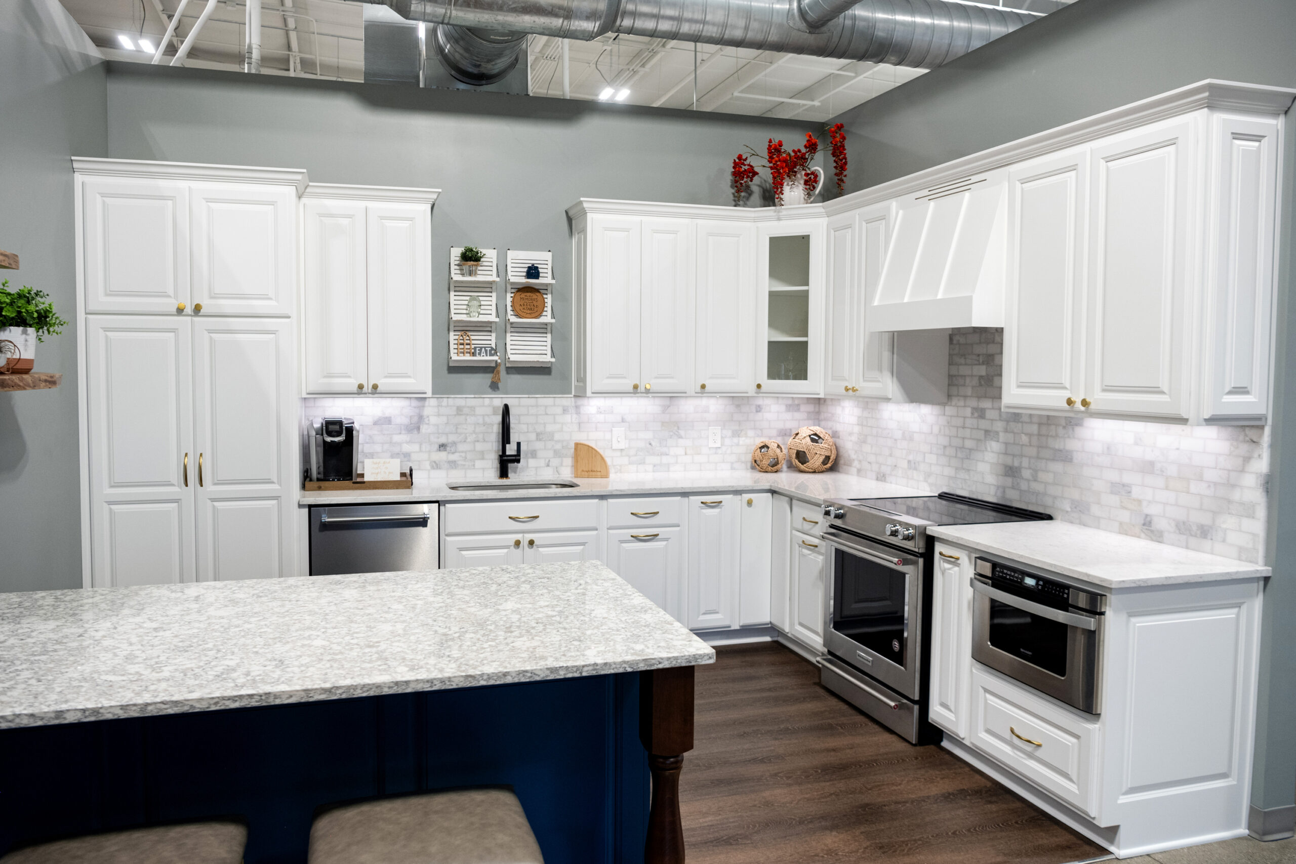 Modern kitchen with white cabinets, marble countertops, stainless steel appliances, and a light gray tile backsplash. Styled shelves and red accents create a fresh look—perfect inspiration from a top kitchen remodeling company Columbus Ohio.