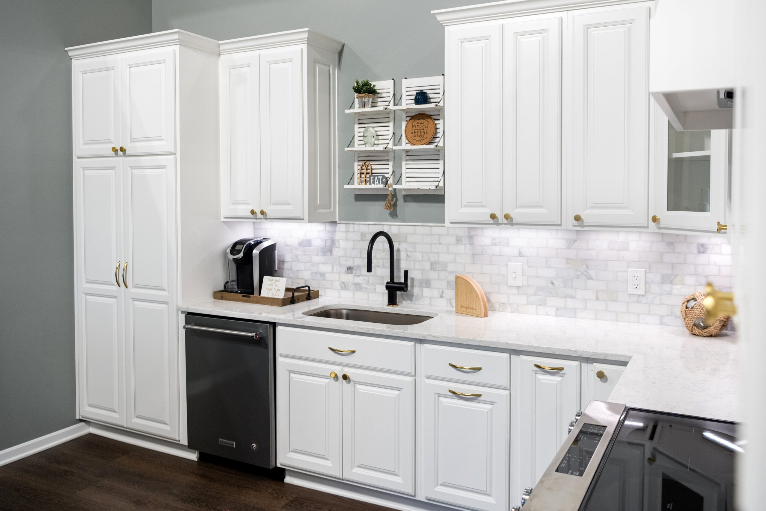 Modern kitchen with white cabinets, marble backsplash, black faucet, stainless steel appliances, dark wood floor, and open shelves with decor and mugs above the sink—crafted with the same attention to detail as a top bathroom remodeling company Columbus Ohio.