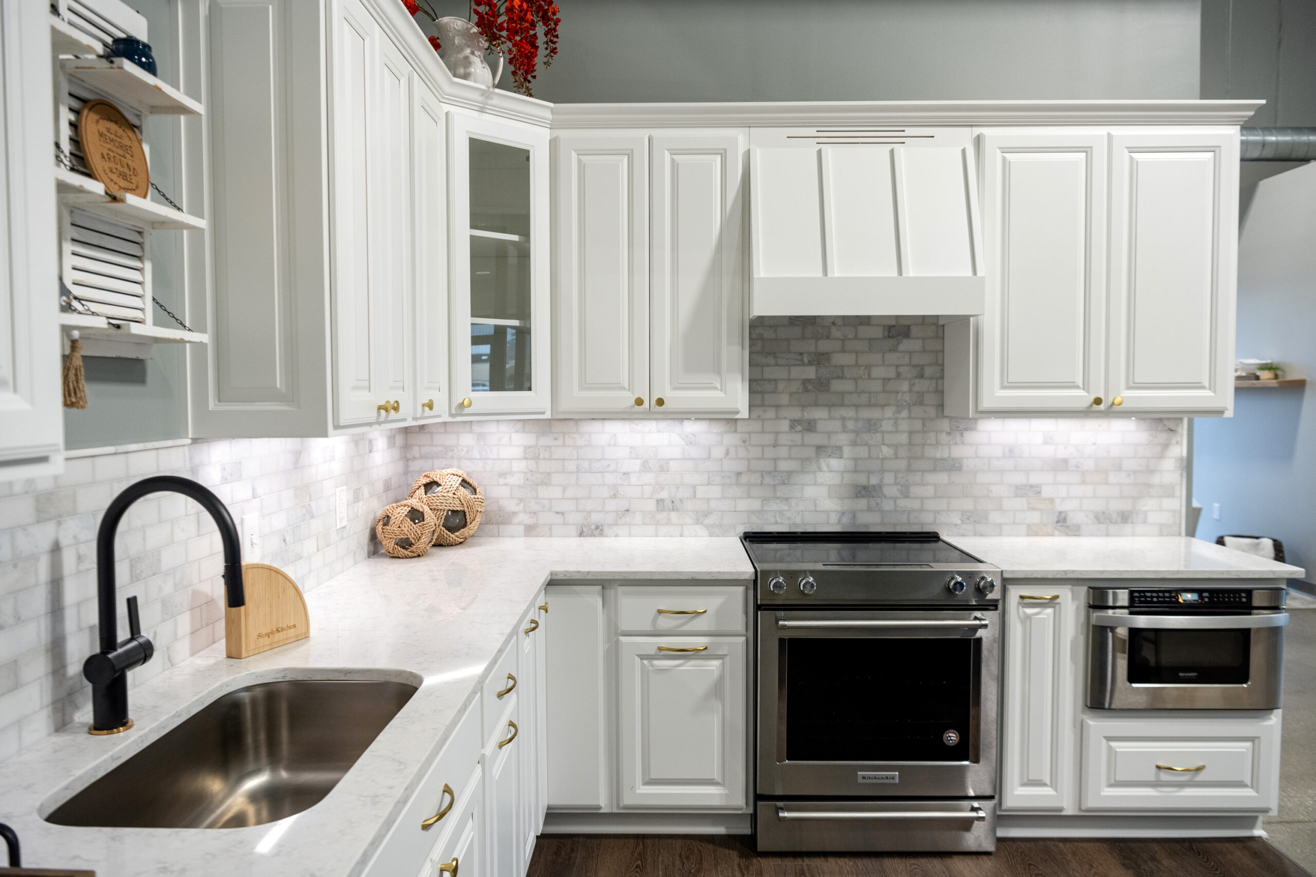 Modern kitchen with white cabinets, stainless steel oven and microwave, marble countertops and backsplash, black sink, gold handles, and decorative items—expertly designed by a top kitchen remodeling company in Columbus, Ohio.