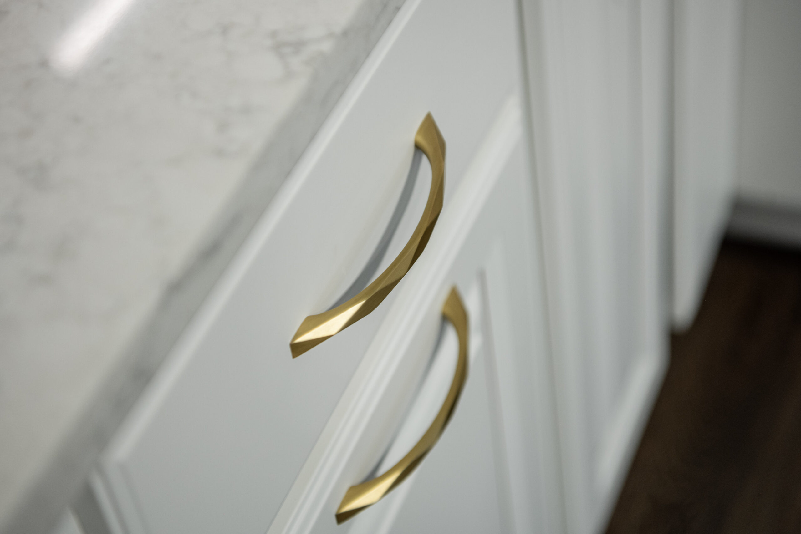 Close-up of two white cabinet drawers with modern, gold handles under a white marble countertop. The dark brown wood floor adds contrast—a stylish touch from a leading kitchen remodeling company in Columbus, Ohio.