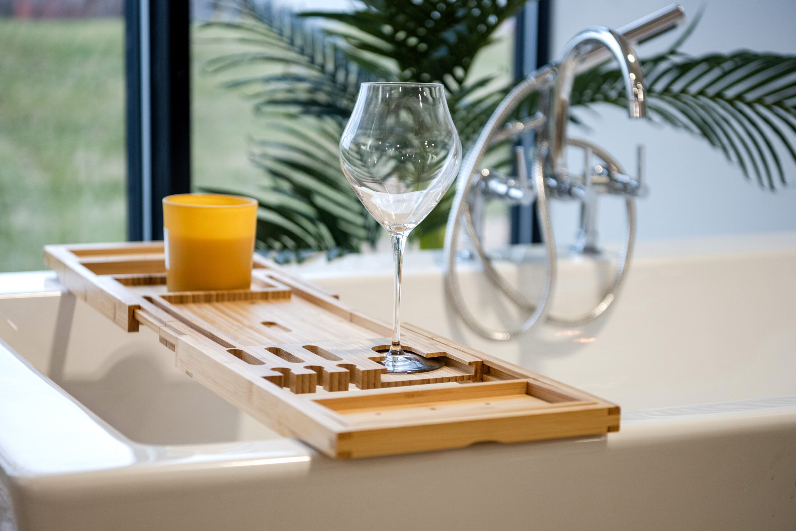 A bathtub with a bamboo tray holding an empty wine glass and a yellow cup, set in a bright space. A chrome faucet and green plant hint at the fresh bathroom renovation by a top bathroom remodeling company Columbus Ohio.