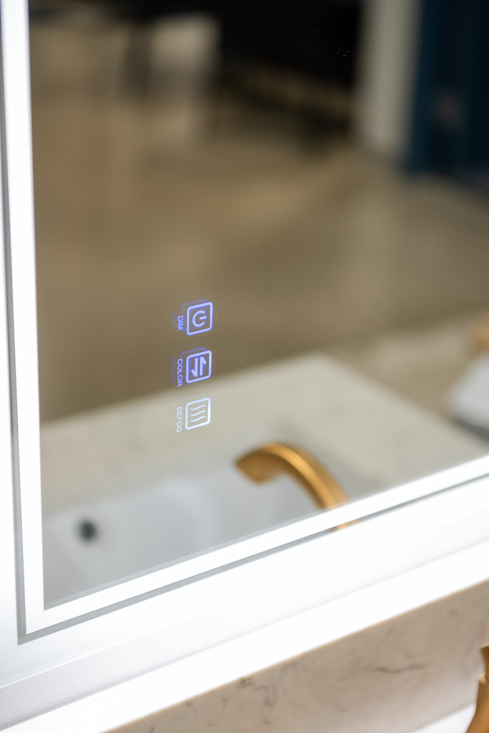 A close-up of a modern bathroom mirror with three illuminated touch buttons, reflected above a white sink and gold faucet on a marble countertop—perfect inspiration for your next kitchen remodel or bathroom upgrade.
