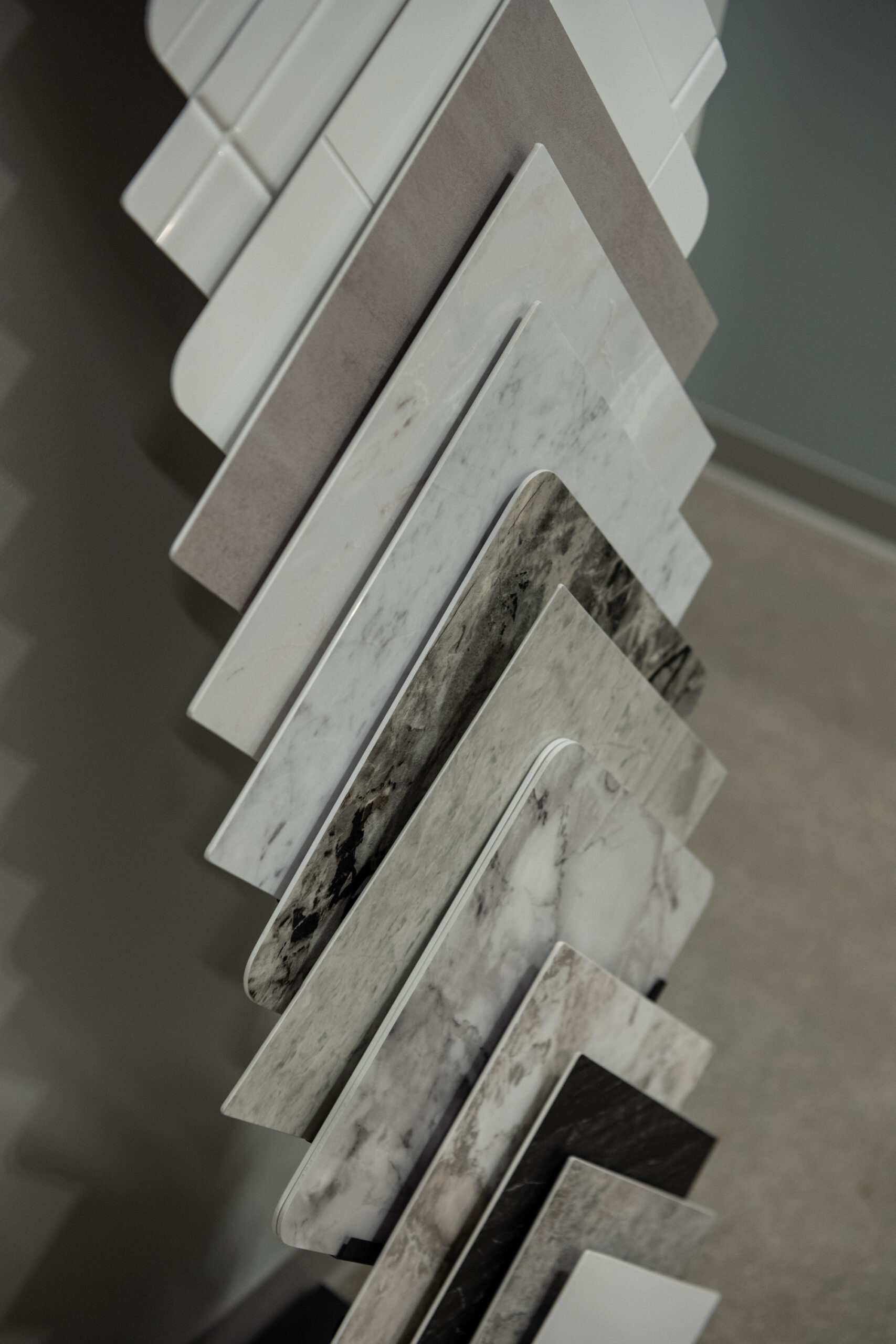 Several rectangular samples of countertop or flooring materials in white, gray, and marble patterns are displayed vertically—perfect inspiration for your next kitchen remodel or bath remodel project.