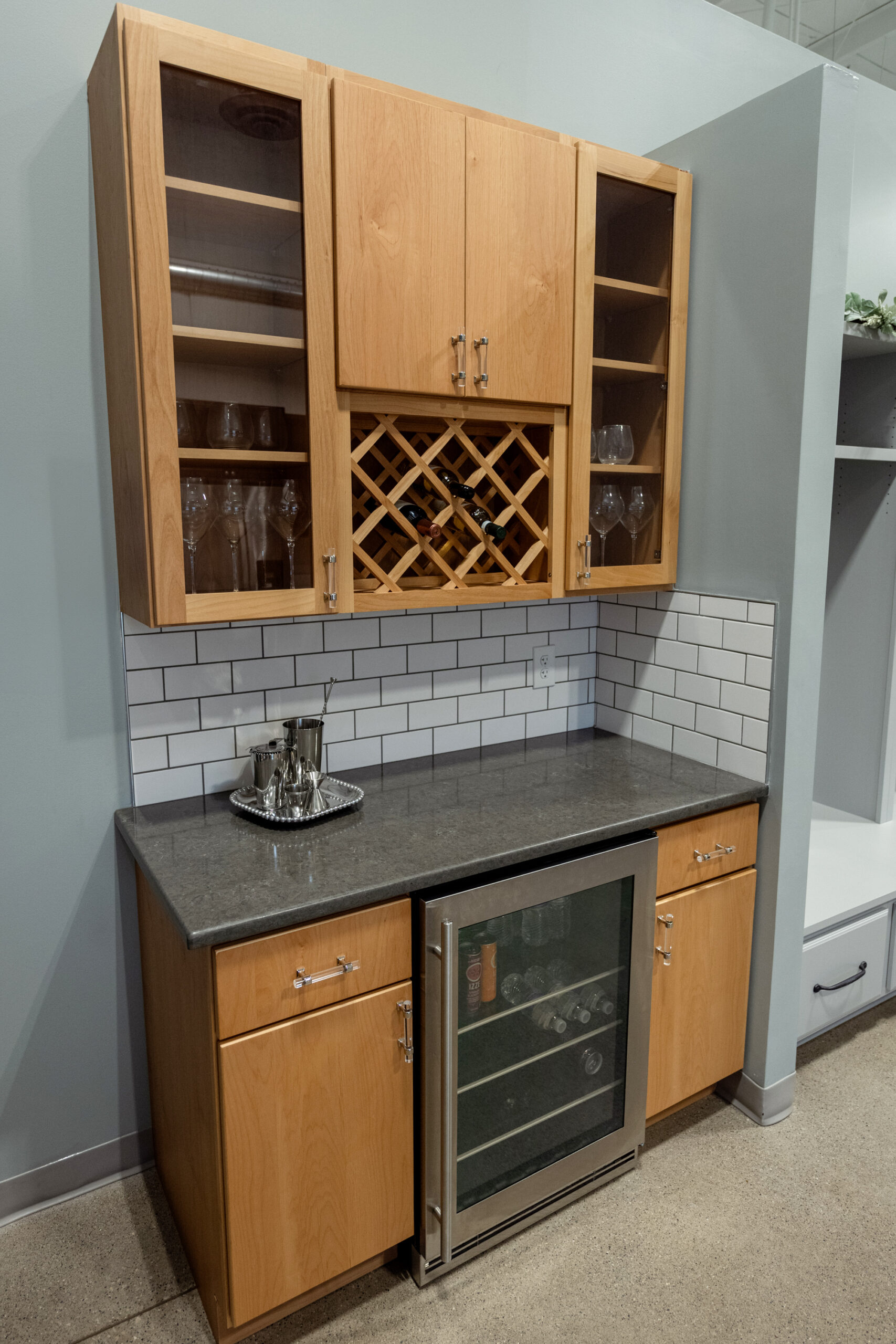 A small home bar area showcases light wood cabinets, a wine rack, glass-front cabinets, a subway tile backsplash, and a mini fridge—perfect inspiration for your next kitchen renovation with a trusted kitchen remodeling company in Columbus, Ohio.