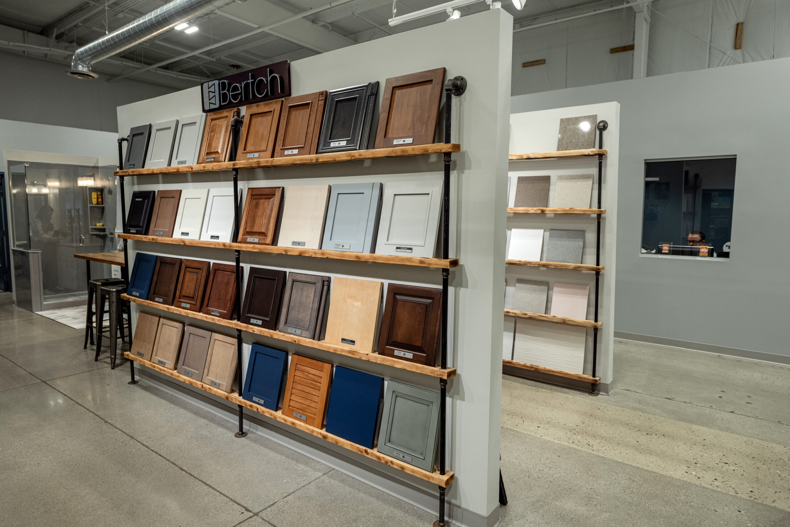 Display wall with shelves showing a variety of cabinet door samples in different colors and finishes, perfect for anyone planning a kitchen remodel in a modern showroom with polished concrete floors.