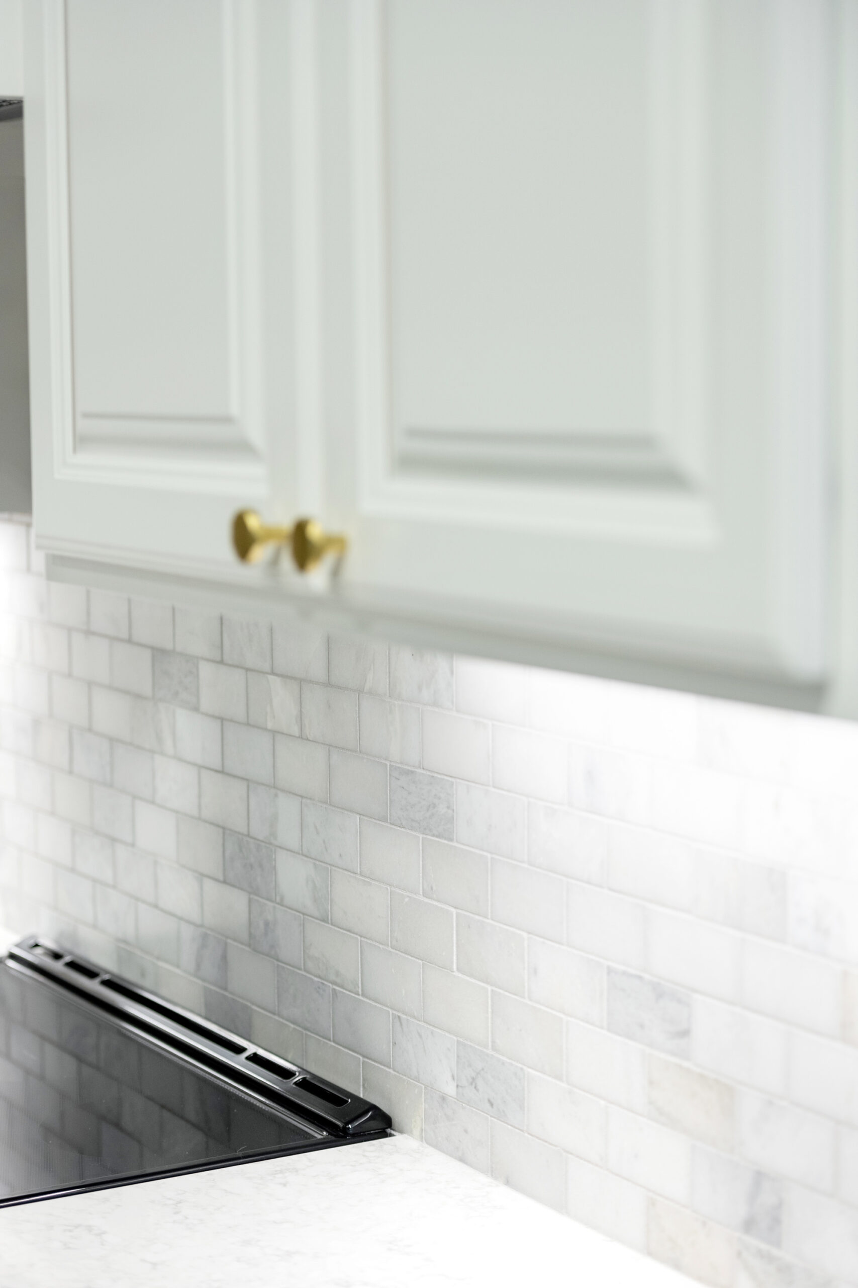 White kitchen cabinets with gold knobs are mounted above a countertop and stove, with white subway tile backsplash. This clean, modern design is an inspiration from a top kitchen remodeling company Columbus Ohio homeowners trust.