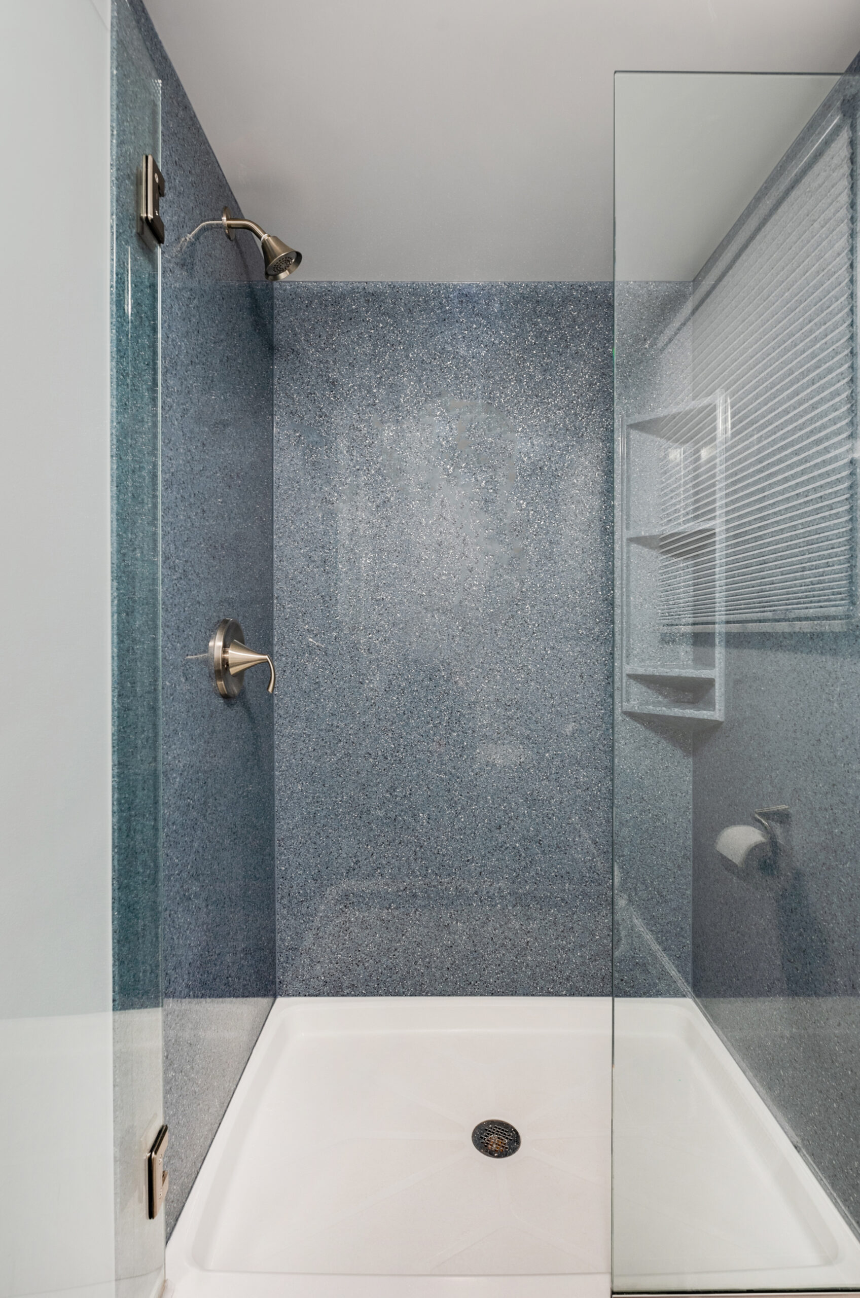 Modern shower with blue speckled walls, a glass door, stainless steel fixtures, a white shower base, and a window with blinds—perfect inspiration for your next bath remodel with a top bathroom remodeling company in Columbus, Ohio.