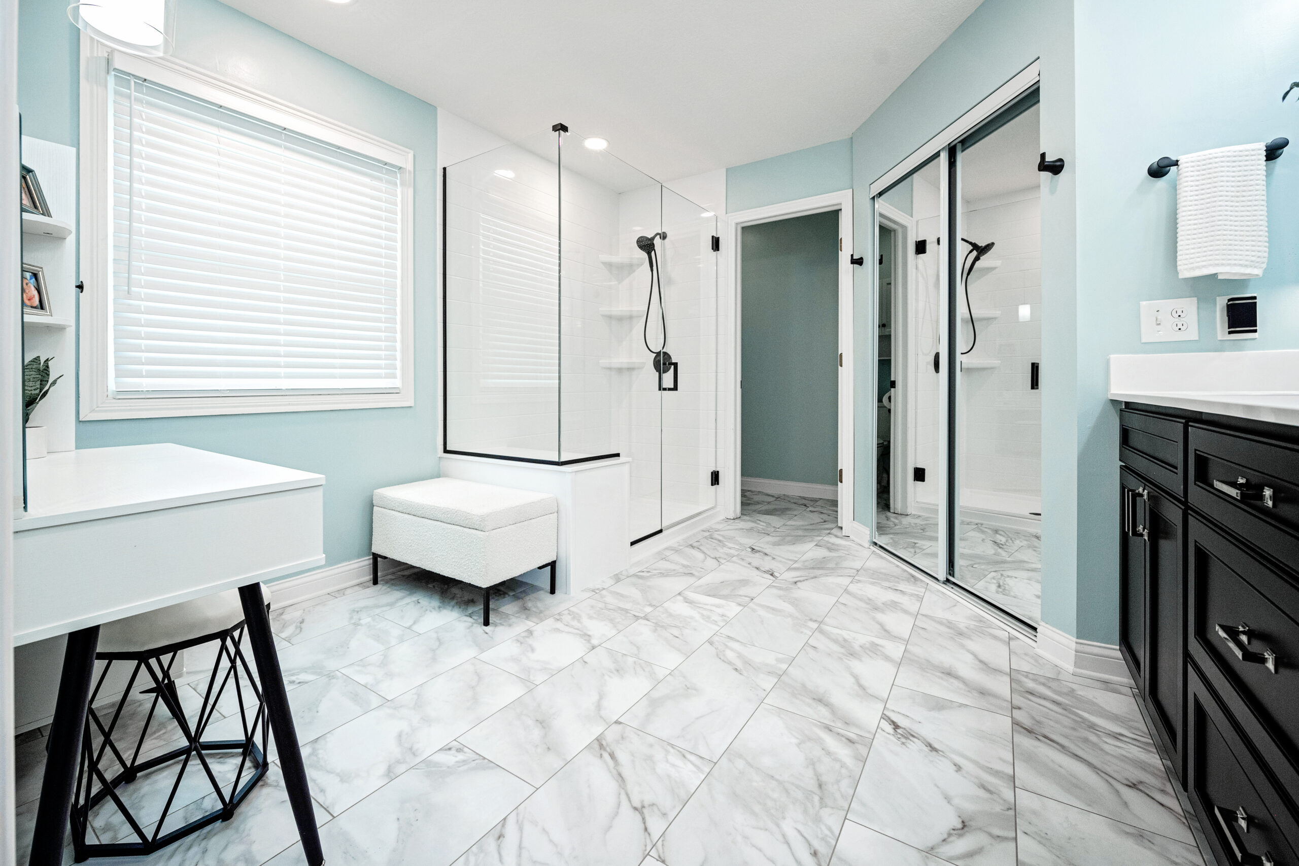 Modern bathroom with marble tile floors, glass shower enclosure, double vanity with black cabinets, and a white makeup vanity; a stunning bath remodel by a top kitchen remodeling company Columbus Ohio. Light blue walls and large mirror complete the look.